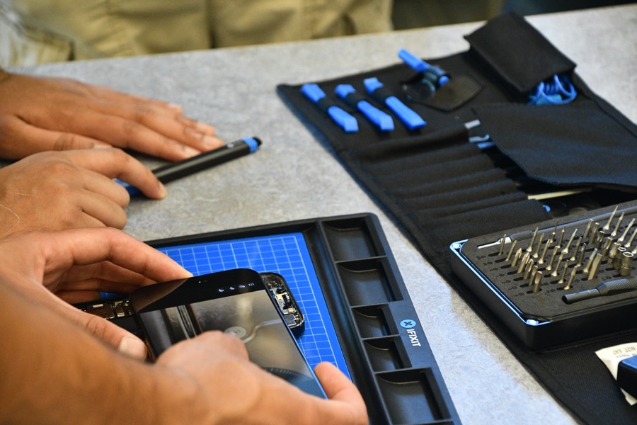 Hands opening a device with picks and drivers on a repair mat