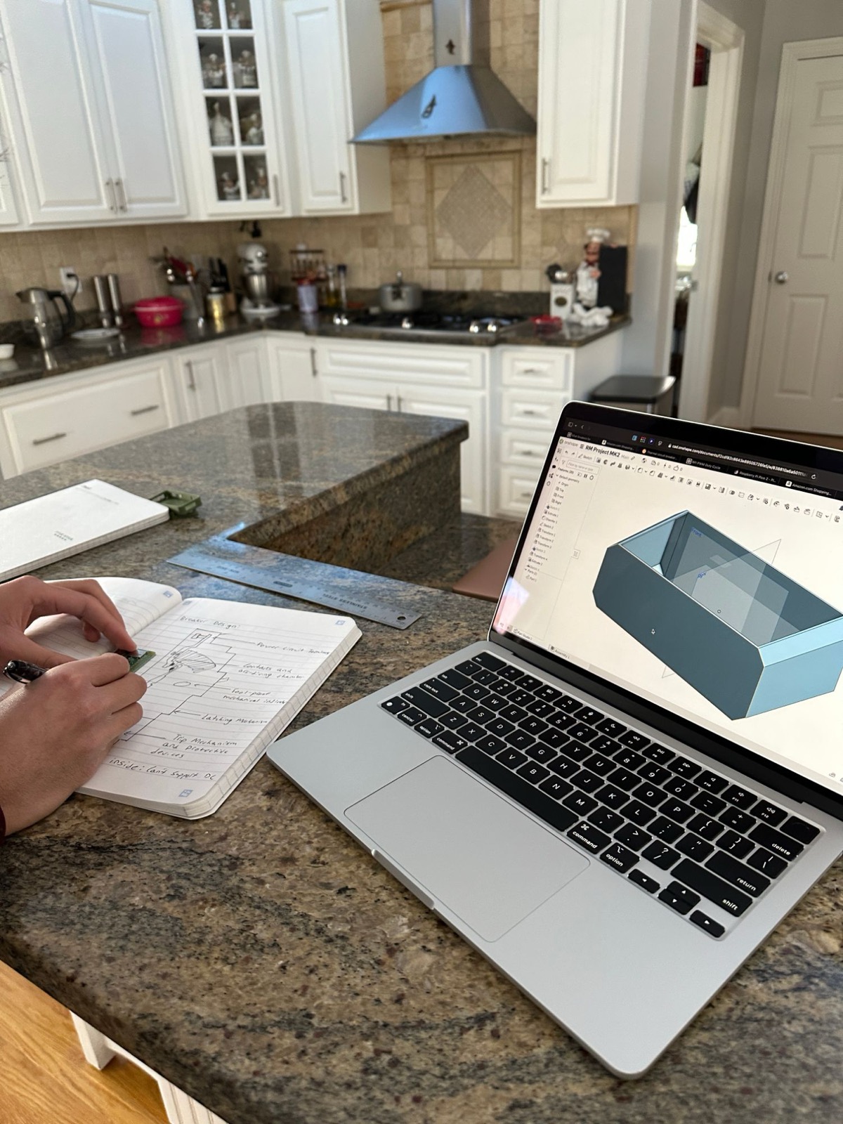 Sketching a breaker design in a notebook beside a laptop running Onshape CAD