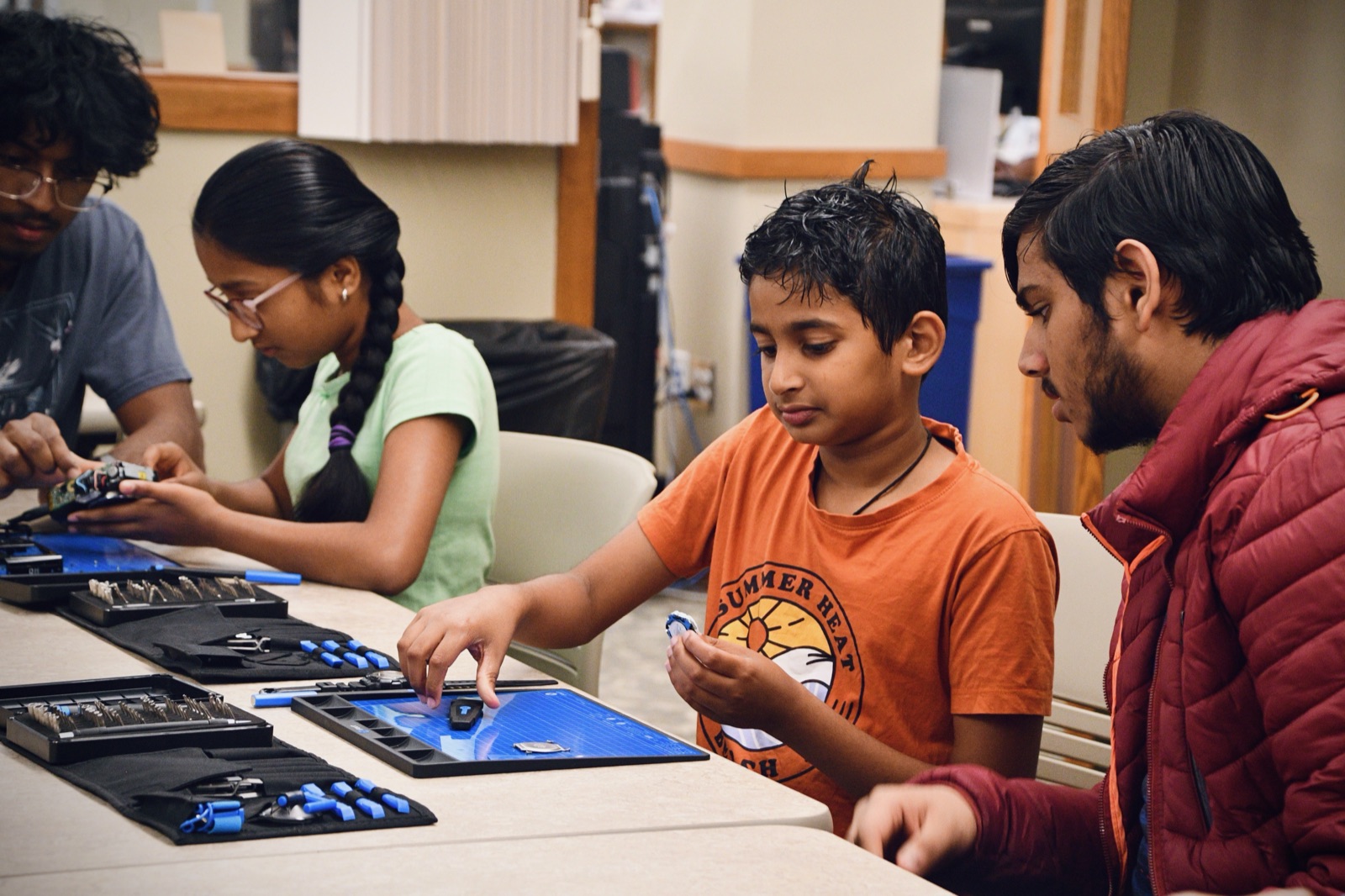 Four students at a workshop table working through repairs with iFixit toolkits